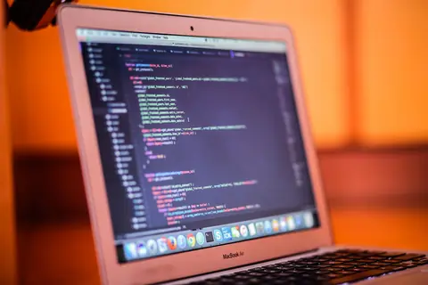 A laptop showing code on a desk lit warm orange