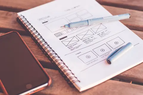 Wireframe sketches in a notebook beside a phone